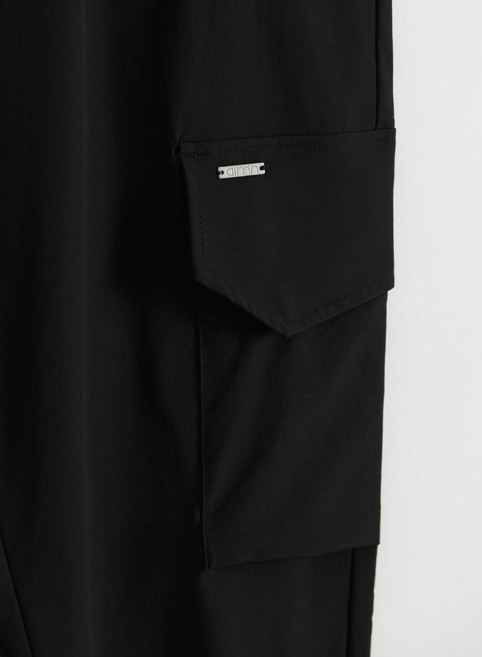 Close-up of black cargo pants showing a flap cargo pocket with an aim'n logo