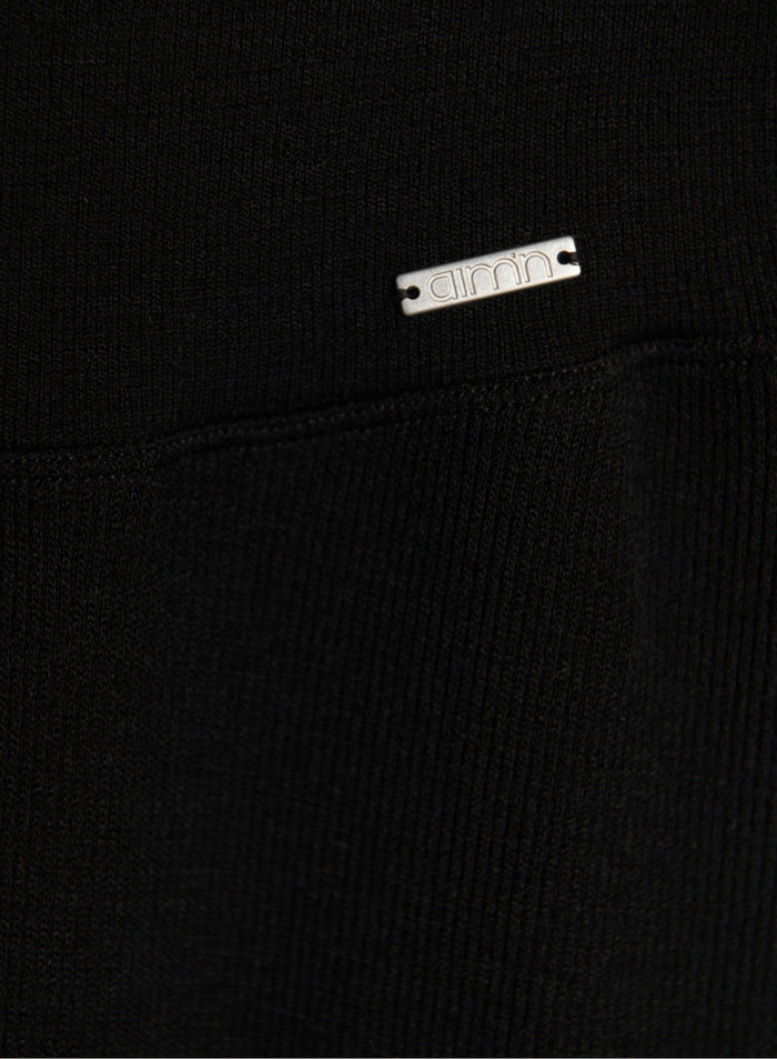 Silver aim'n logo badge detail on black ribbed wool blend knit fabric.