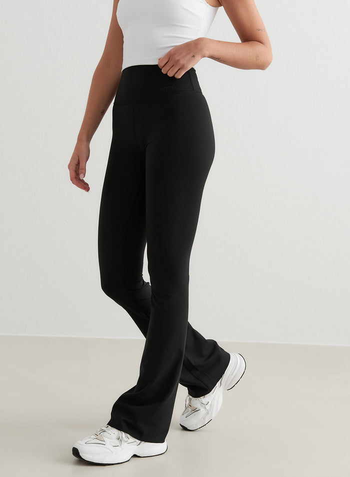 High-waisted black aim'n Sense Flare Tights featuring a flared leg and buttery-soft fabric, paired with white sneakers.