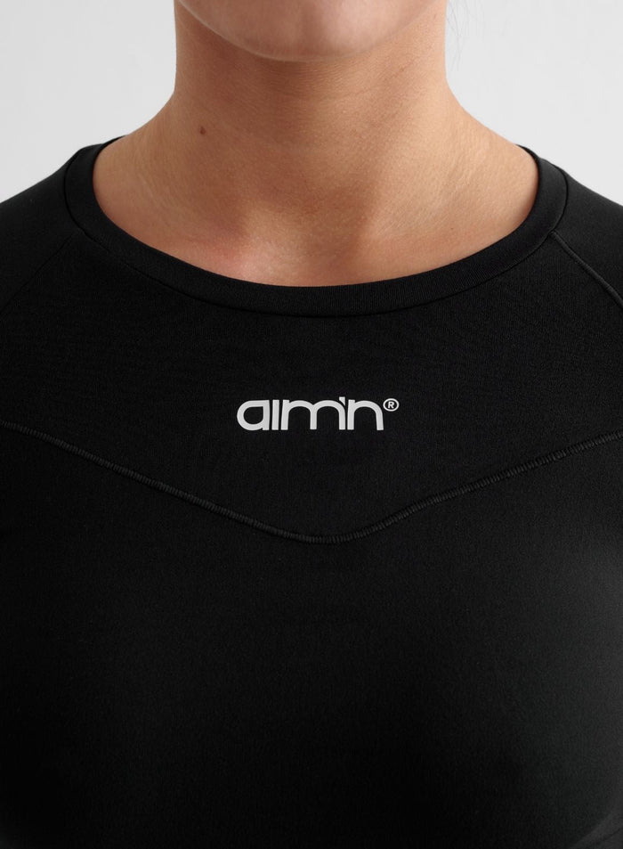 Close-up of a black Soft Basic Long Sleeve featuring a white aim'n logo and pintuck detailing.