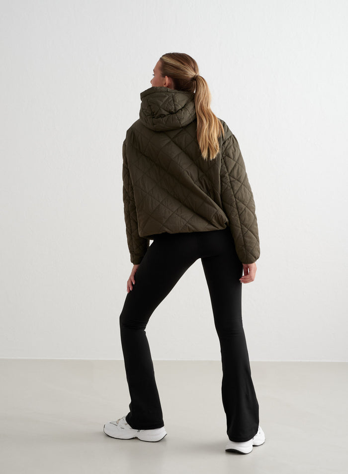 Rear view of black Warming Flare Tights paired with an olive green quilted jacket from aim'n. [S-175cm]