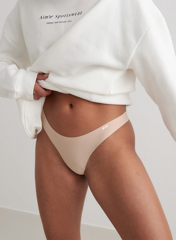 Model wearing a nude Beige Invisible Thong and a white sweatshirt by aim'n