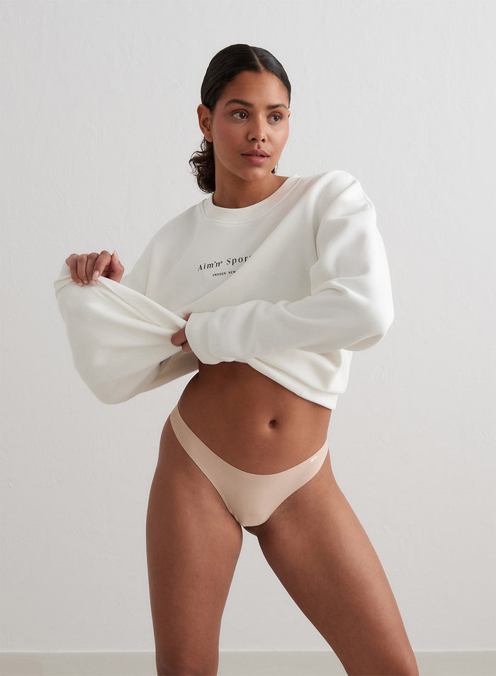 Model wearing a nude Beige Invisible Thong from aim'n and lifting up a white sweatshirt