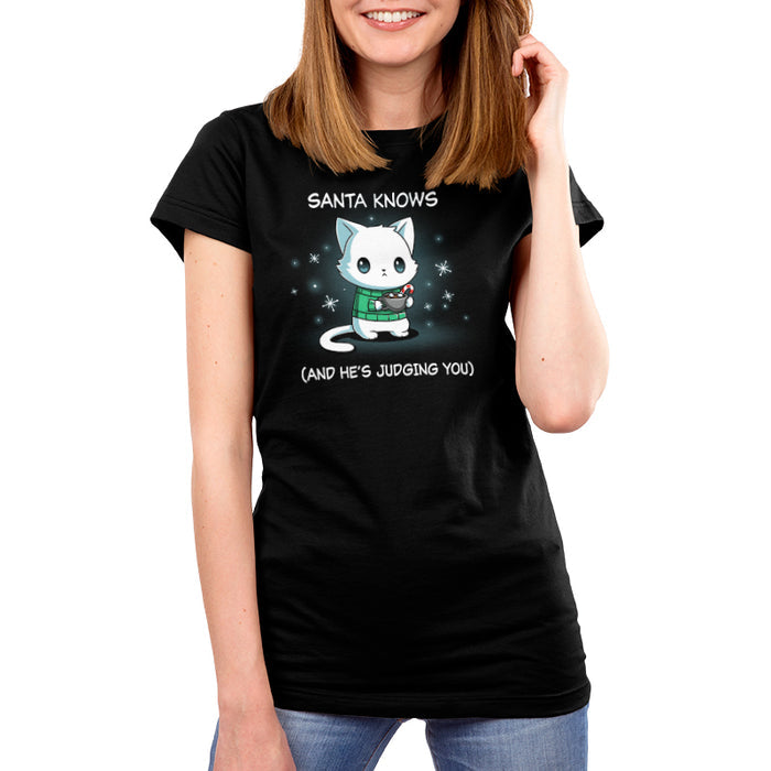 Premium Cotton T-shirt_TeeTurtle black Santa Knows apparel featuring a cat with a deadpan expression holding mug with hot chocolate, marshmallows, and a candy cane surrounded by snowflakes, with the caption, “Santa Knows (And He’s Judging You)“.