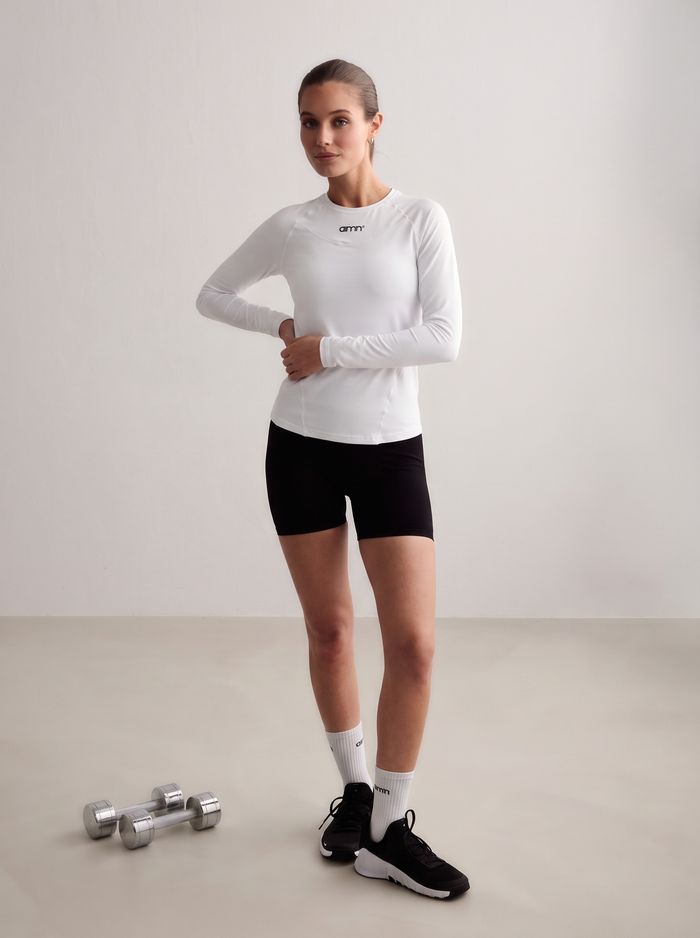 Model wearing a white aim'n Soft Basic Long Sleeve with black shorts and dumbbells [S-174 cm]